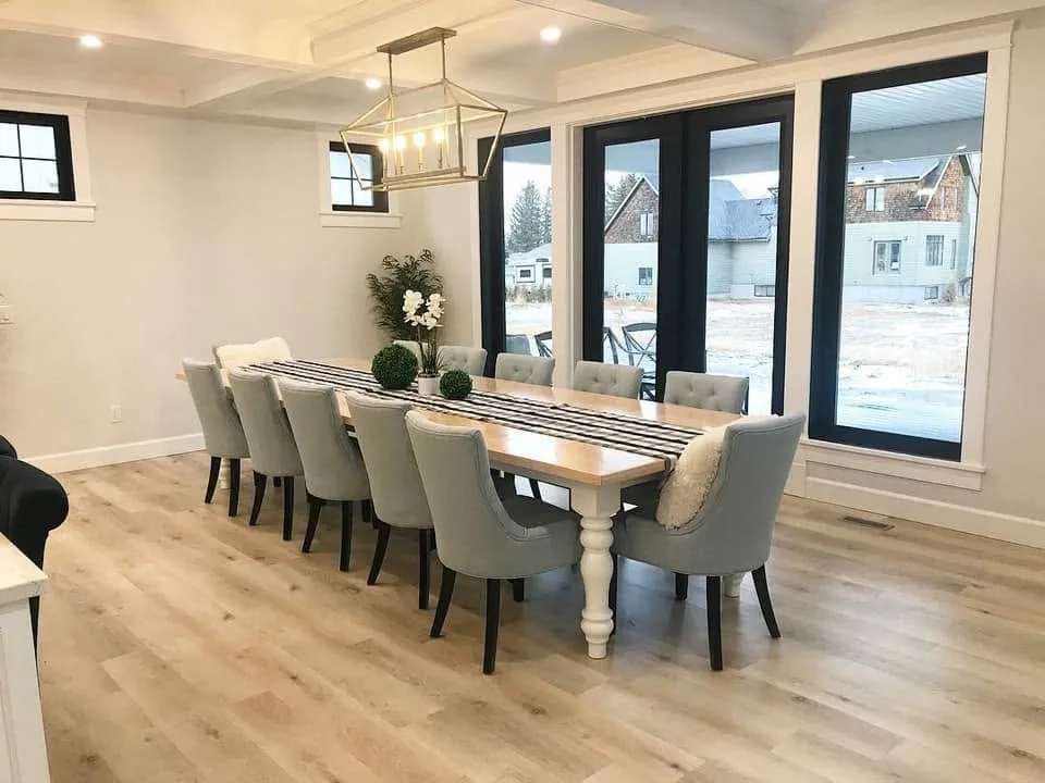 Furnished dining space with a long wood table beside tall dark-trimmed windows