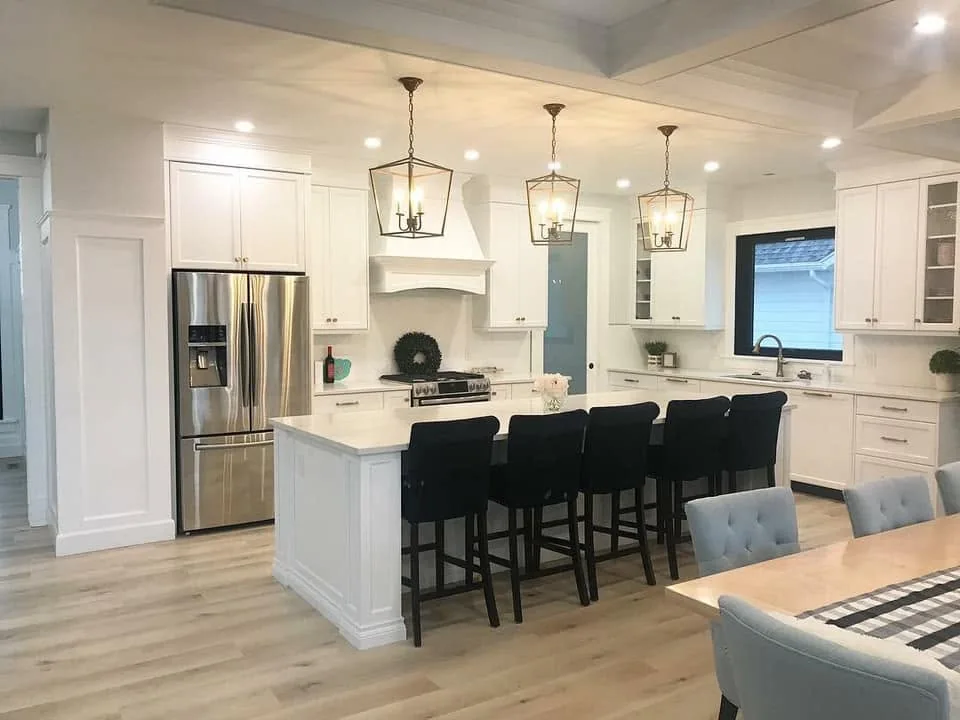 White kitchen with lantern pendants, custom range hood and dark seating at the island