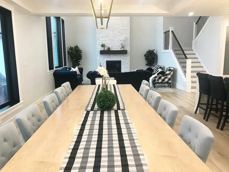 Long dining table with upholstered chairs, opening onto a living room with a white stone fireplace