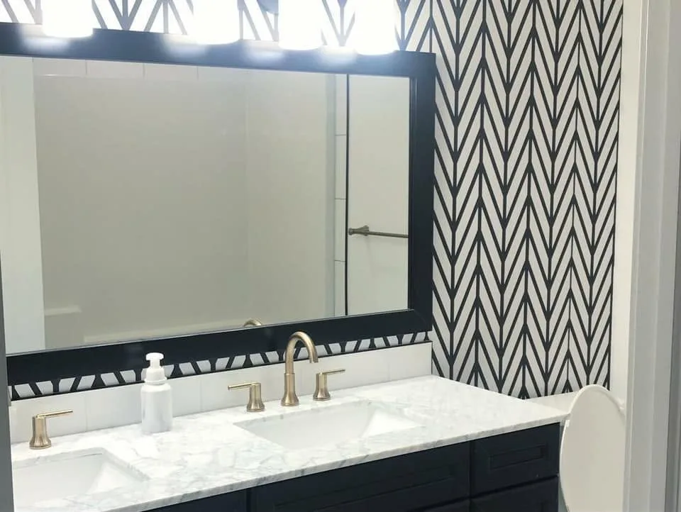 Double vanity with brass faucets against a black-and-white patterned wall