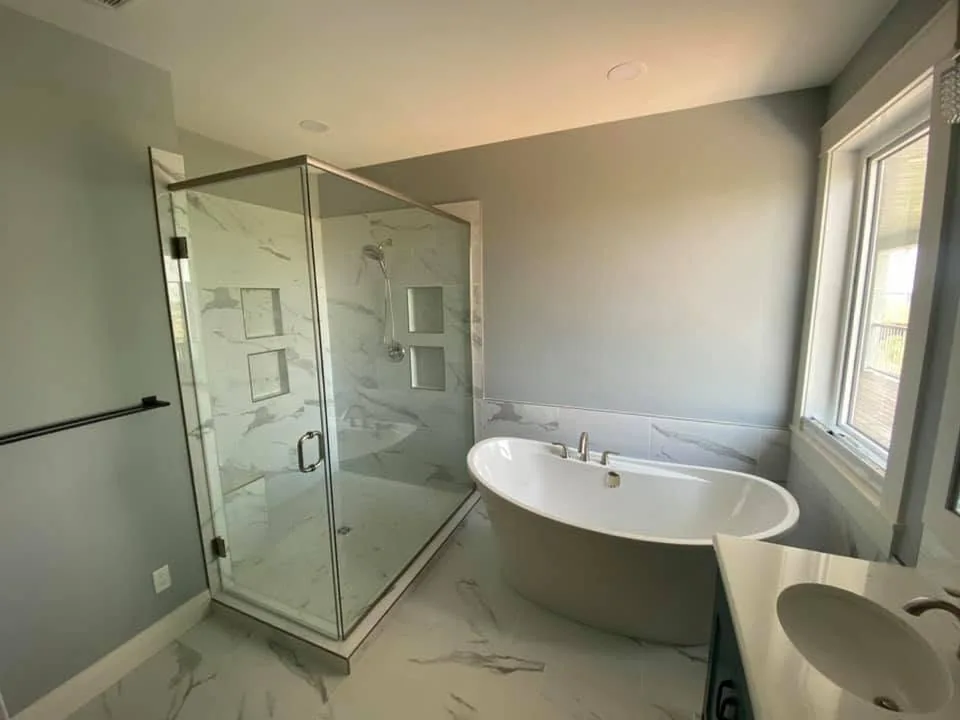 Bathroom with a glass-enclosed shower and a freestanding white tub below a window
