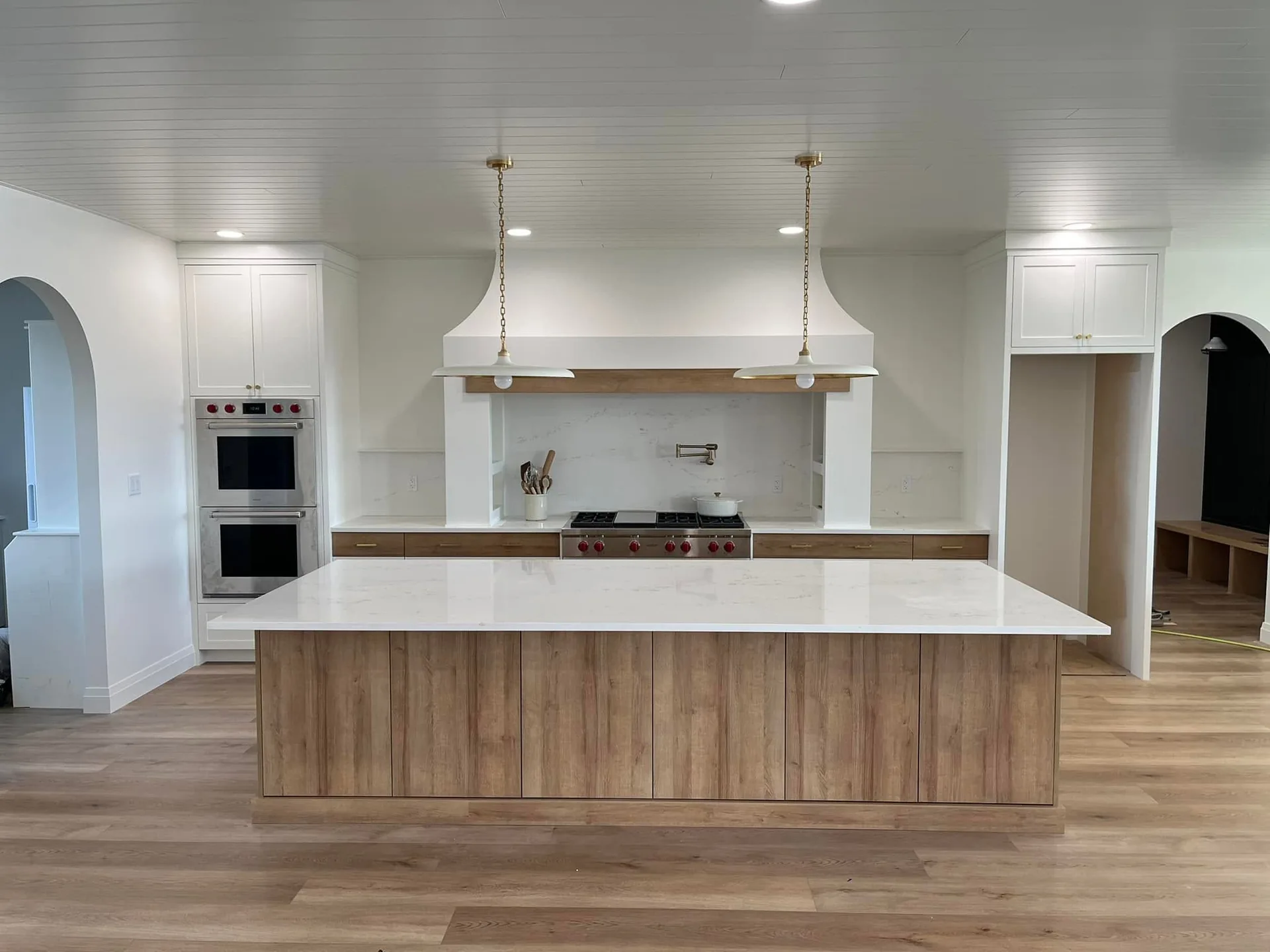 Completed kitchen with a natural wood island, white cabinetry and a wide custom range hood