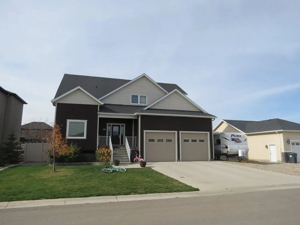 Finished home with grey-green siding, gabled rooflines, double garage and a front lawn
