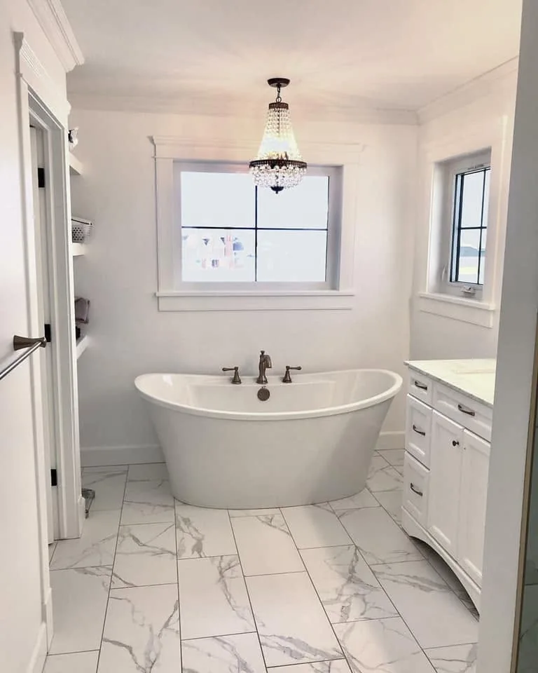 Finished bathroom with a freestanding tub, pale marble-patterned tile and a chandelier