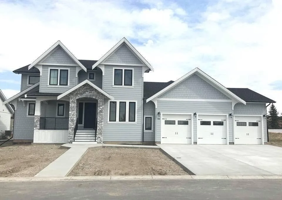 Finished two-storey grey home with gabled rooflines, stone entrance and three garage doors