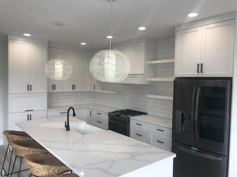 Bright white kitchen with a veined island countertop, dark appliances and woven stools