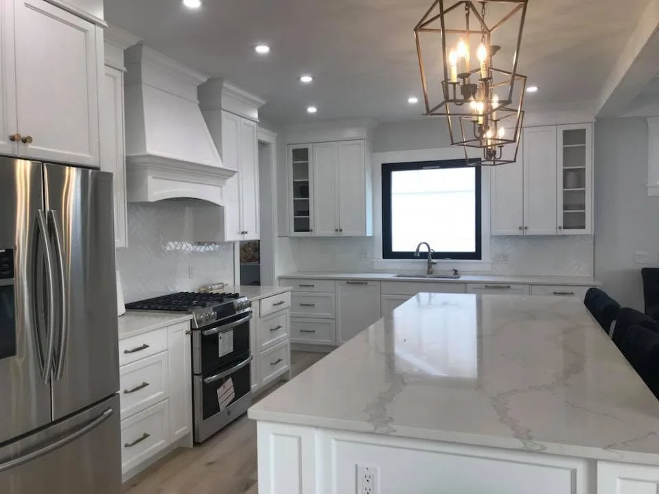Finished white kitchen with a veined island surface, lantern lighting and a custom range hood
