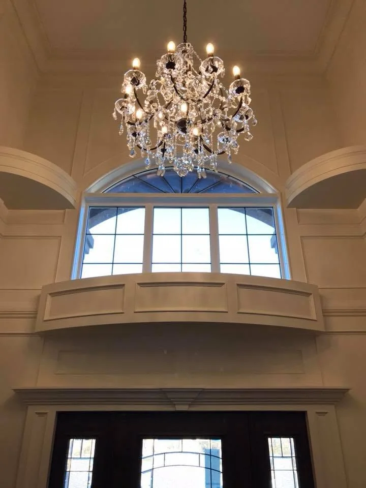 Crystal chandelier above an arched entry window and detailed white wall panelling