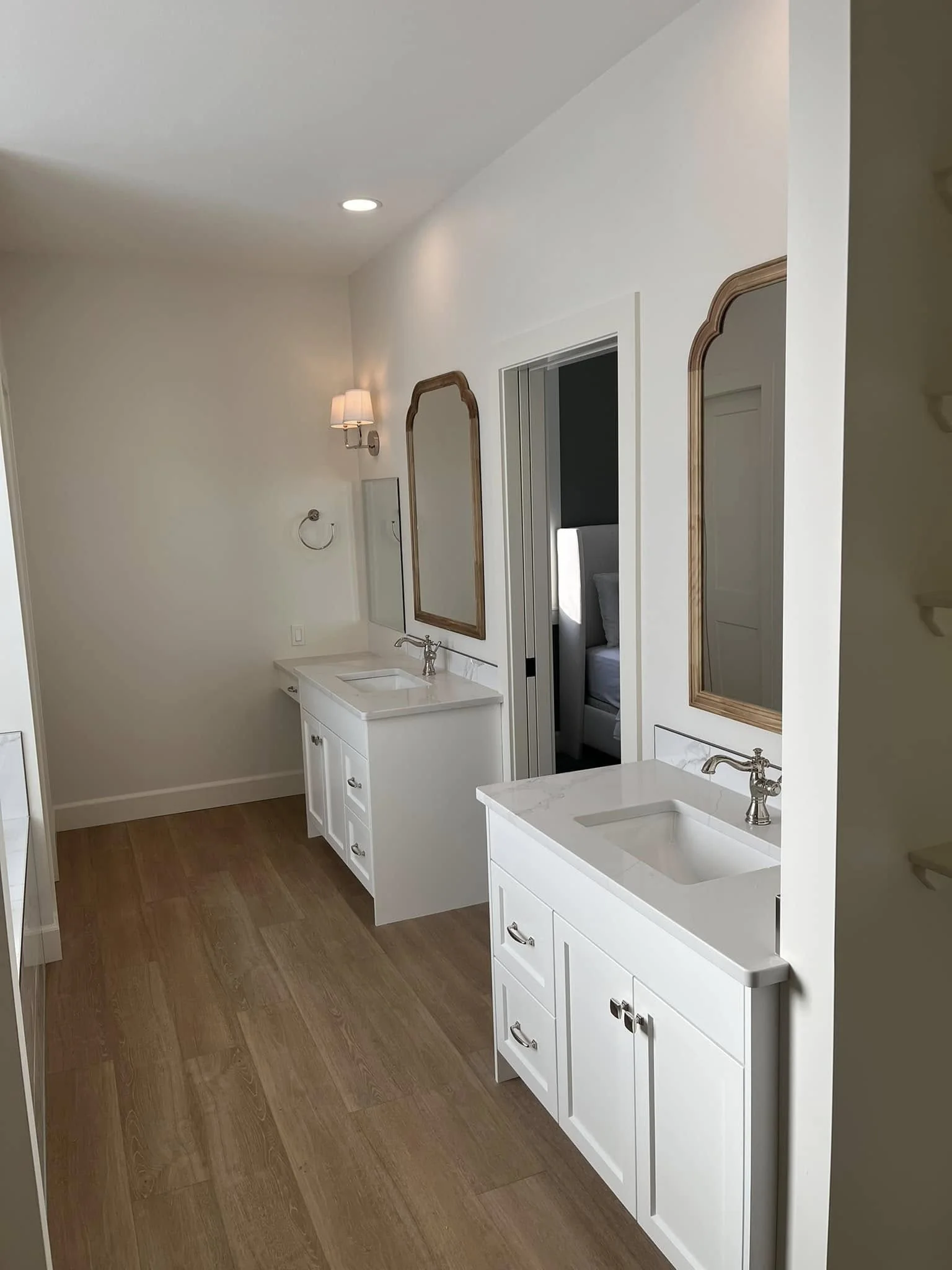 White bathroom vanities with warm metal-framed mirrors and wood-look flooring