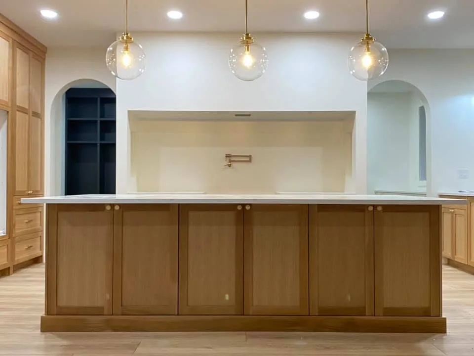 Natural wood kitchen island beneath glass pendants, with arched openings behind