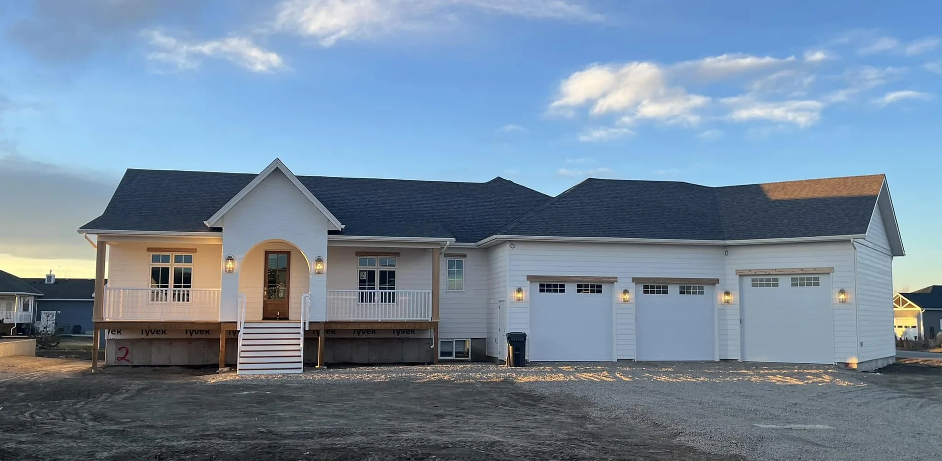 White home at dusk with an arched porch entrance, three garage doors and unfinished landscaping