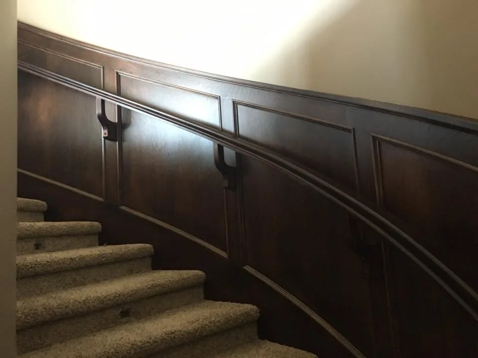 Curved staircase with dark timber wall panelling and a matching handrail