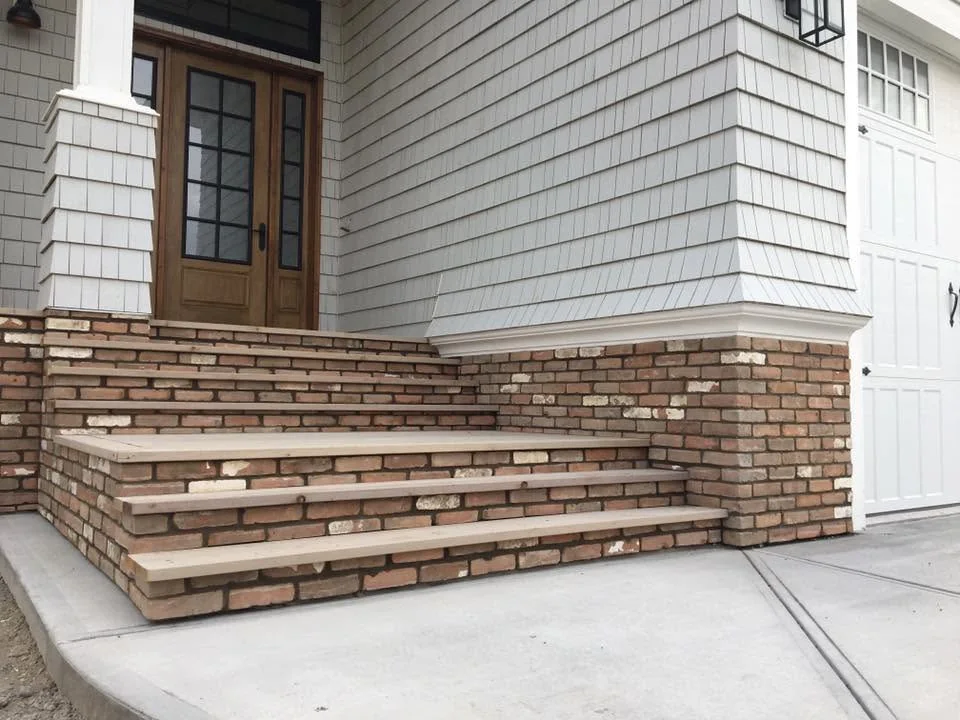 Brick entrance steps beneath a wood door, shingle siding and lantern lighting