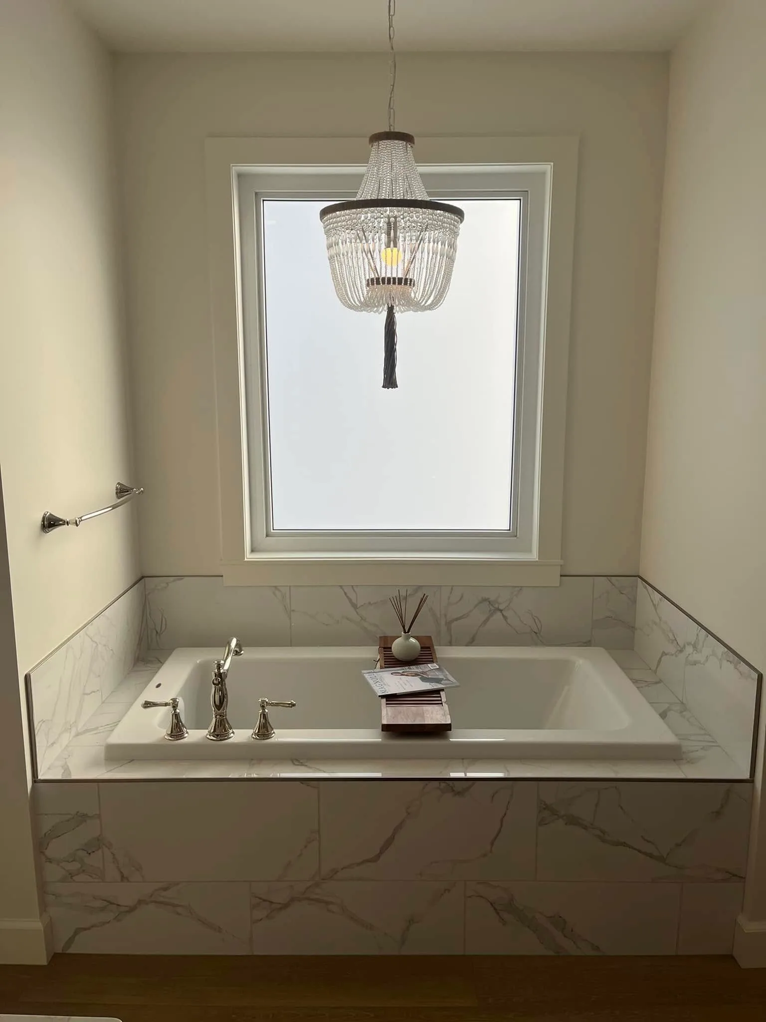 Beaded chandelier above a marble-tiled soaker tub and a tall window