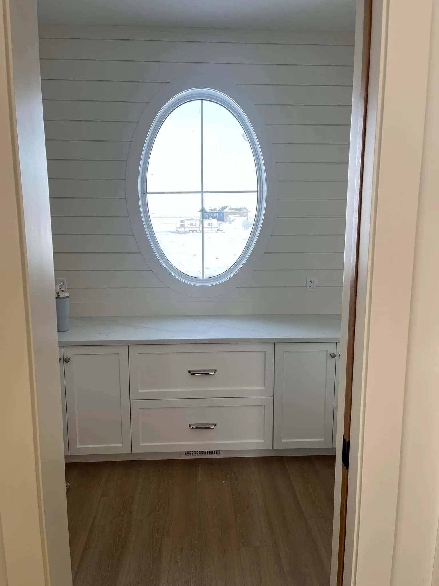 Oval window set into a shiplap wall above white cabinetry and a quartz counter