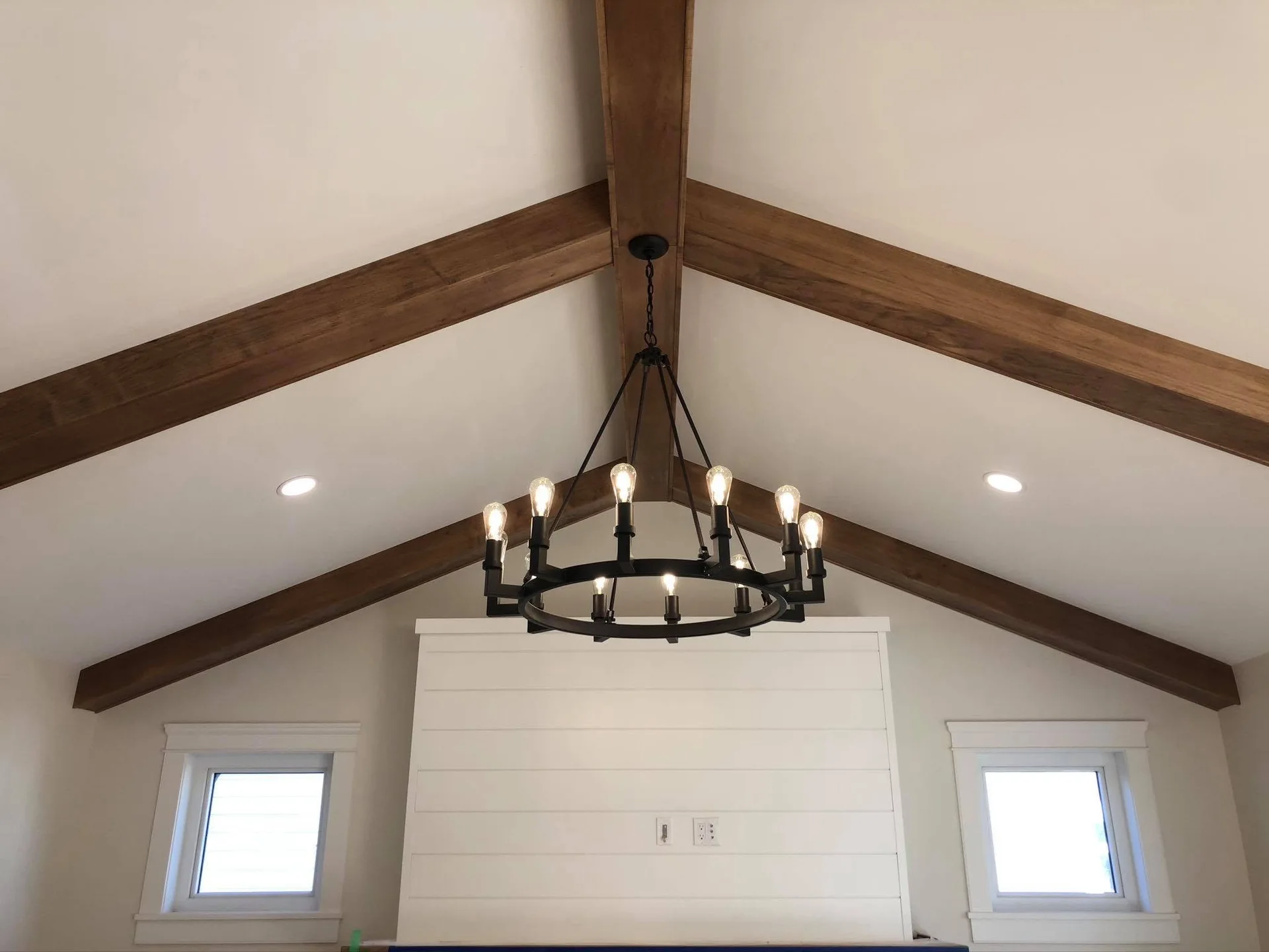 Close view of exposed timber beams and a ring chandelier along a vaulted ceiling
