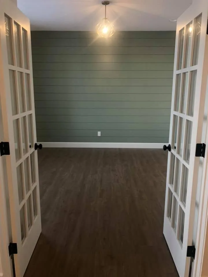 Glass French doors opening into a den with a green shiplap wall