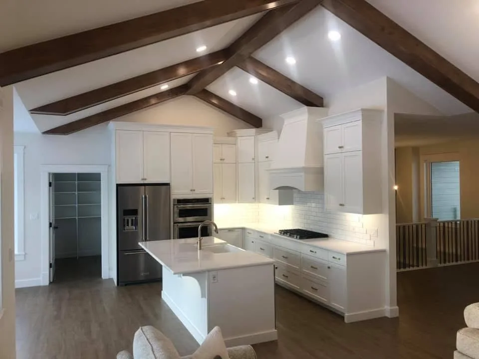 White island kitchen under a vaulted ceiling crossed by dark timber beams