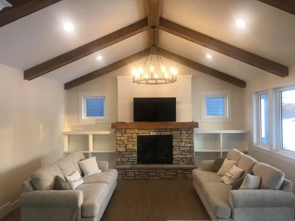 Furnished living room beneath dark exposed beams with a stone fireplace and white shelving