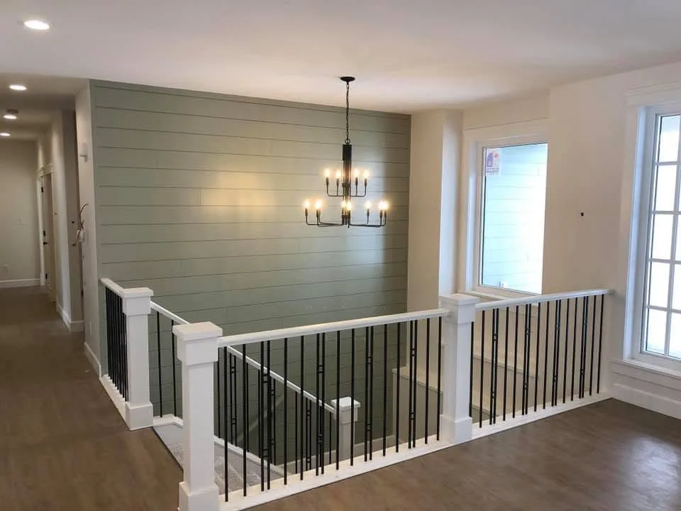 Open stair with black balusters beside a green shiplap feature wall